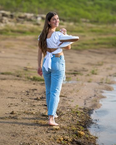 Girl holding tennis shoes walking near lake