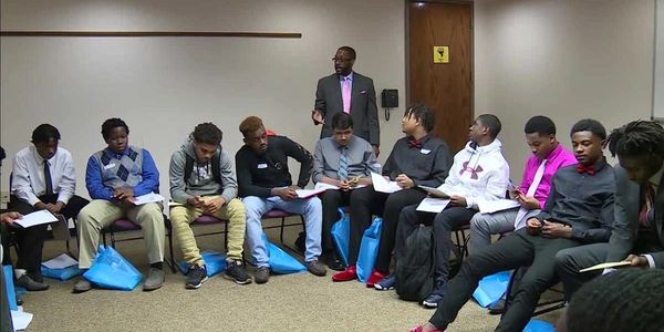 A group of young men in formal attire sitting in a circle with a speaker standing.