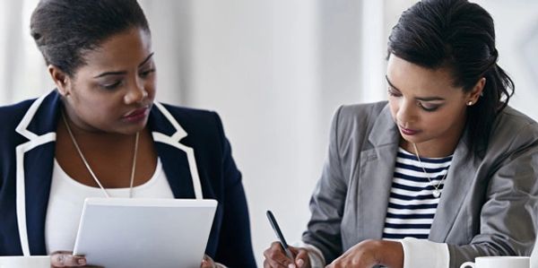 Two professional women reviewing documents in a meeting.