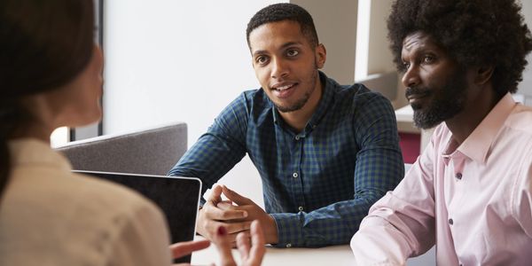 Three professionals engaged in a business discussion around a table.