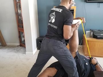 A man stretching another man's leg using a resistance band indoors.