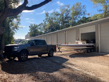 Pickup truck towing a boat outside storage units on a sunny day.