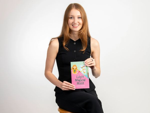 Young woman in black holding a book titled 'Lily's Magical Mind'.