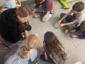 Group of kids and an adult working on a project with marshmallows and sticks.