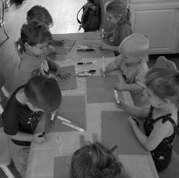 Children drawing with markers around a table in a classroom.