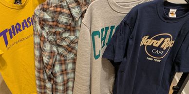 Four casual shirts hanging, including a yellow Thrasher tee and a Hard Rock Cafe tee.