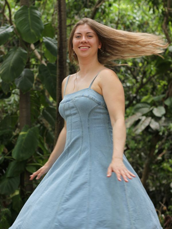 Woman in a blue dress twirling outdoors among lush greenery.