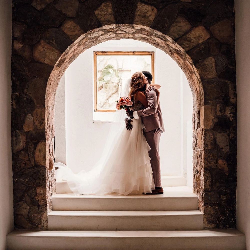 Bride and groom embrace under a stone archway, bathed in soft light.