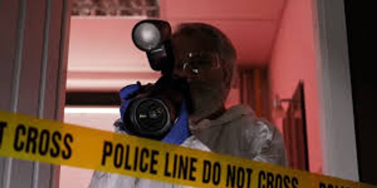 Photographer taking pictures behind police line tape in a dimly lit room.