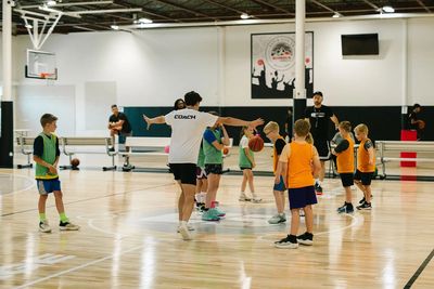 Coach instructing kids during basketball practice on indoor court.