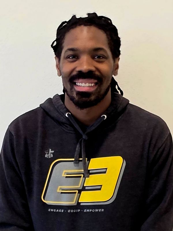 Smiling man in a dark hoodie with a yellow and gray logo.