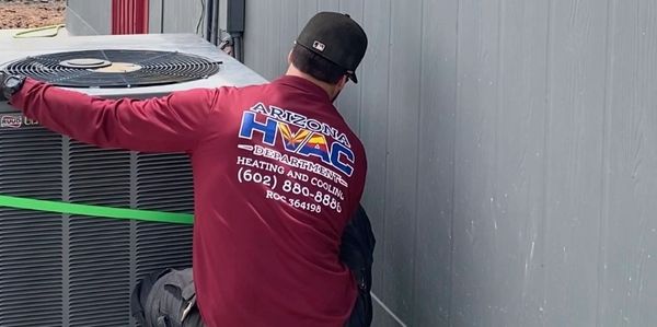HVAC technician installing or servicing an air conditioning unit outside a building.