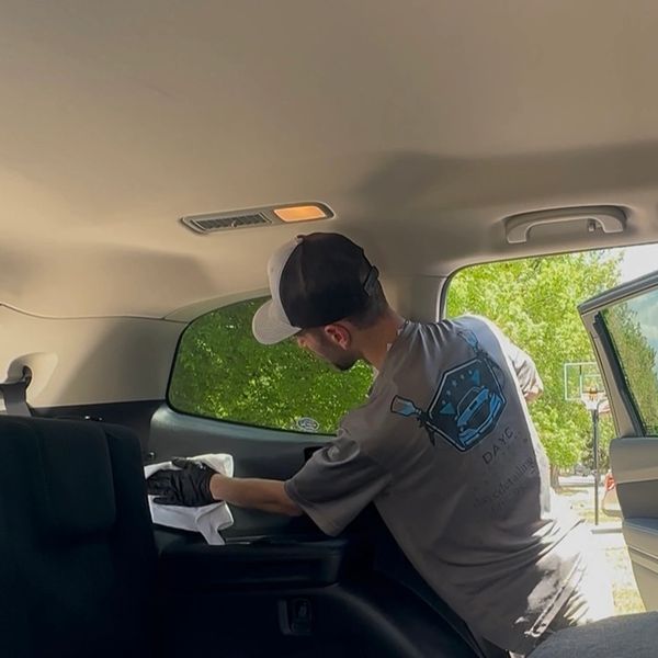 AJ Schaffer, owner of DAYC Detailing, cleaning interior of a car with a towel wearing company gear