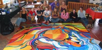 Group of people posing with a large colorful abstract painting on the floor.