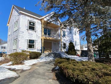 A house under construction with Tyvek wrap and some snow on the ground.