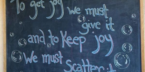 a chalkboard written on with a quote about joy- saying to get it we must scatter it