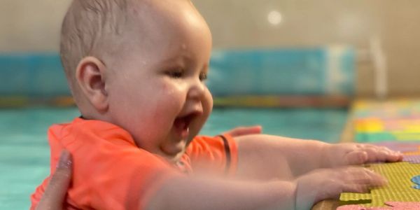 Baby enjoying water play in a pool with support.
