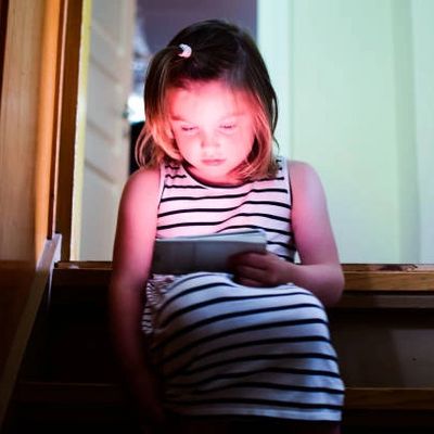 A child's face glowing in the light of a screen alone on stairs.