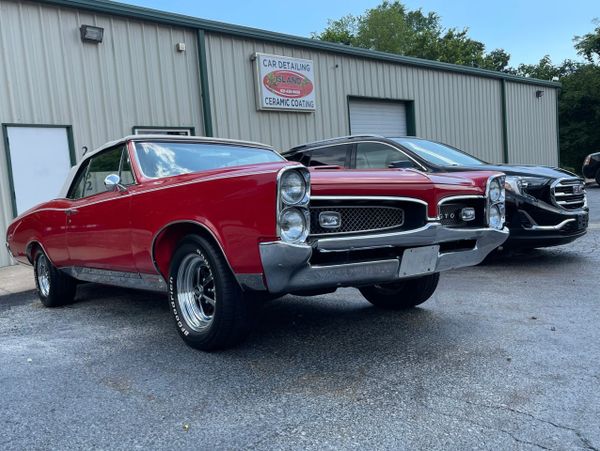 A shiny red classic Pontiac GTO parked outside a car detailing shop.
