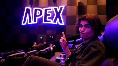 Young man pointing to a glowing APEX sign in a theater.