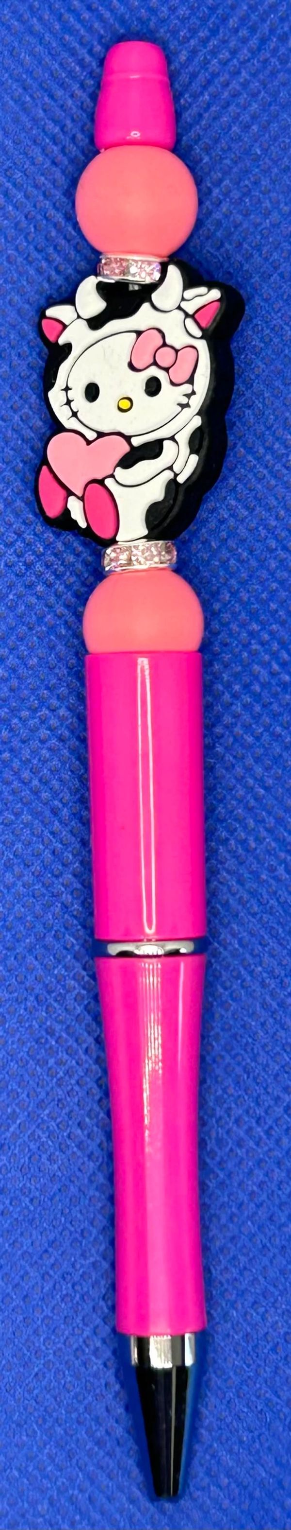 Pink pen with Hello Kitty cow design on a blue surface.