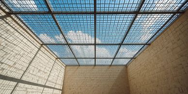 Blue sky and clouds seen through a metal grid ceiling.