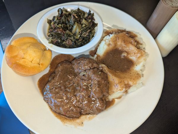 Hamburger steak with mashed potatoes, collard greens and cornbread muffin.