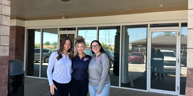 Three women standing closely outside a building.