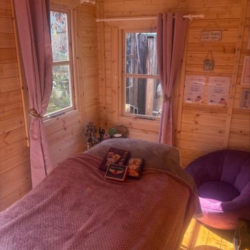 Cozy wooden room with a bed, pink curtains, and a purple chair.