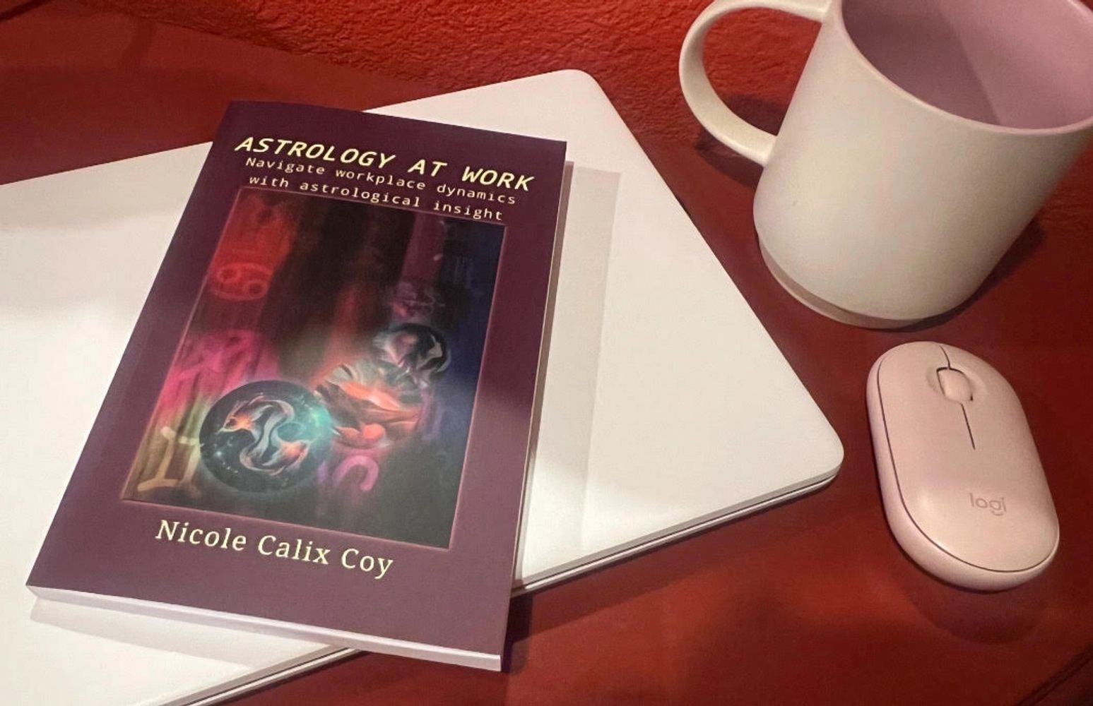 Book titled 'Astrology at Work' on a laptop with a pink mouse and white mug.