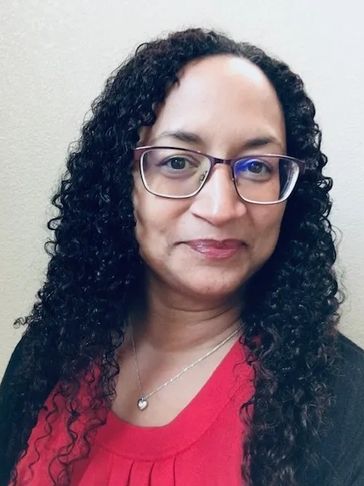 Woman with curly hair and glasses smiling gently.