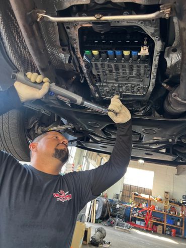 Mechanic using a torque wrench to work on a vehicle's undercarriage in a workshop.