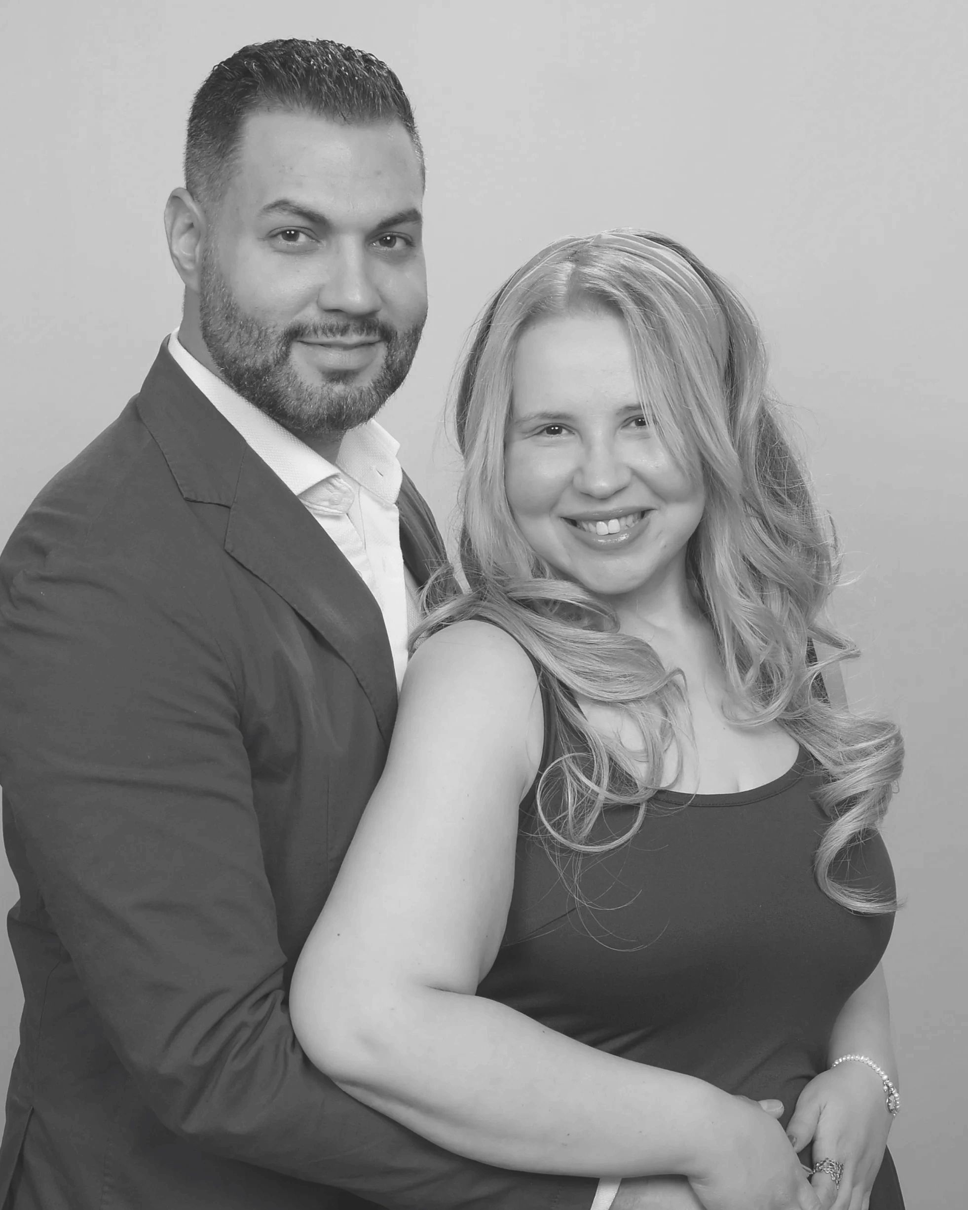 Smiling couple posing closely together in a black and white portrait.