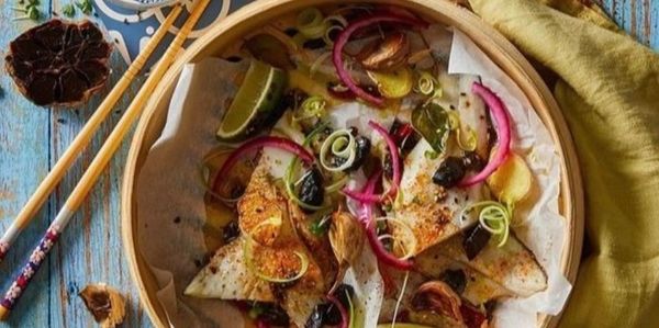 Grilled fish with vibrant garnishes in a bamboo steamer basket.