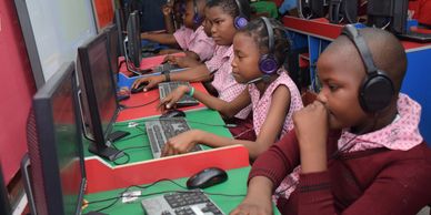 Children focused on computers wearing headphones in a classroom.