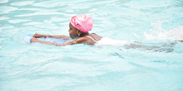 Child practicing swimming with a kickboard in a pool.
