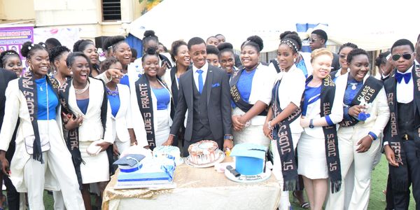 Group of students celebrating with cakes and sashes outdoors.
