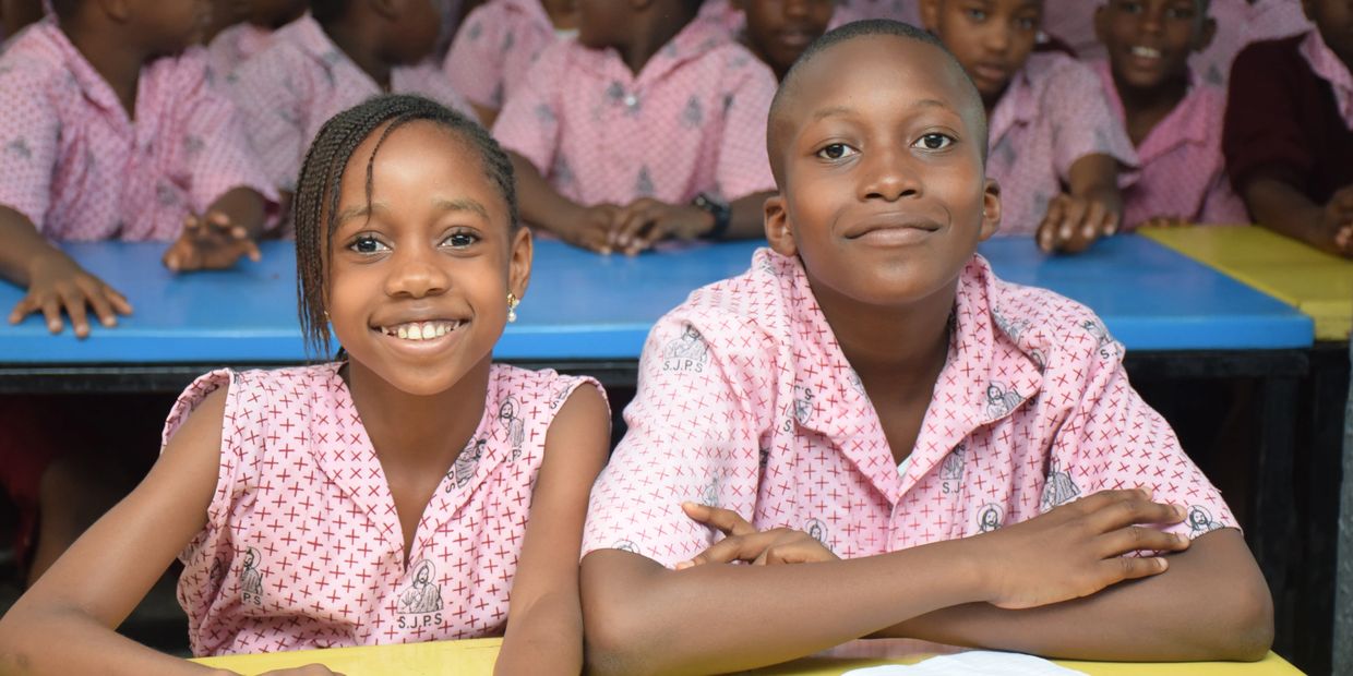 Two smiling children in pink school uniforms sitting at a desk.
