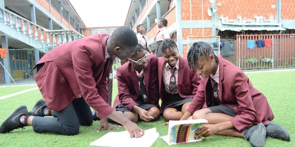 Four students in maroon uniforms study together on a school field.