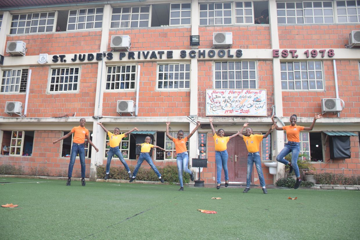 Eight children jump joyfully in front of St. Jude's Private Schools building.