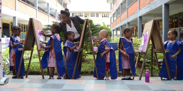 Children painting outdoors with a teacher's guidance.