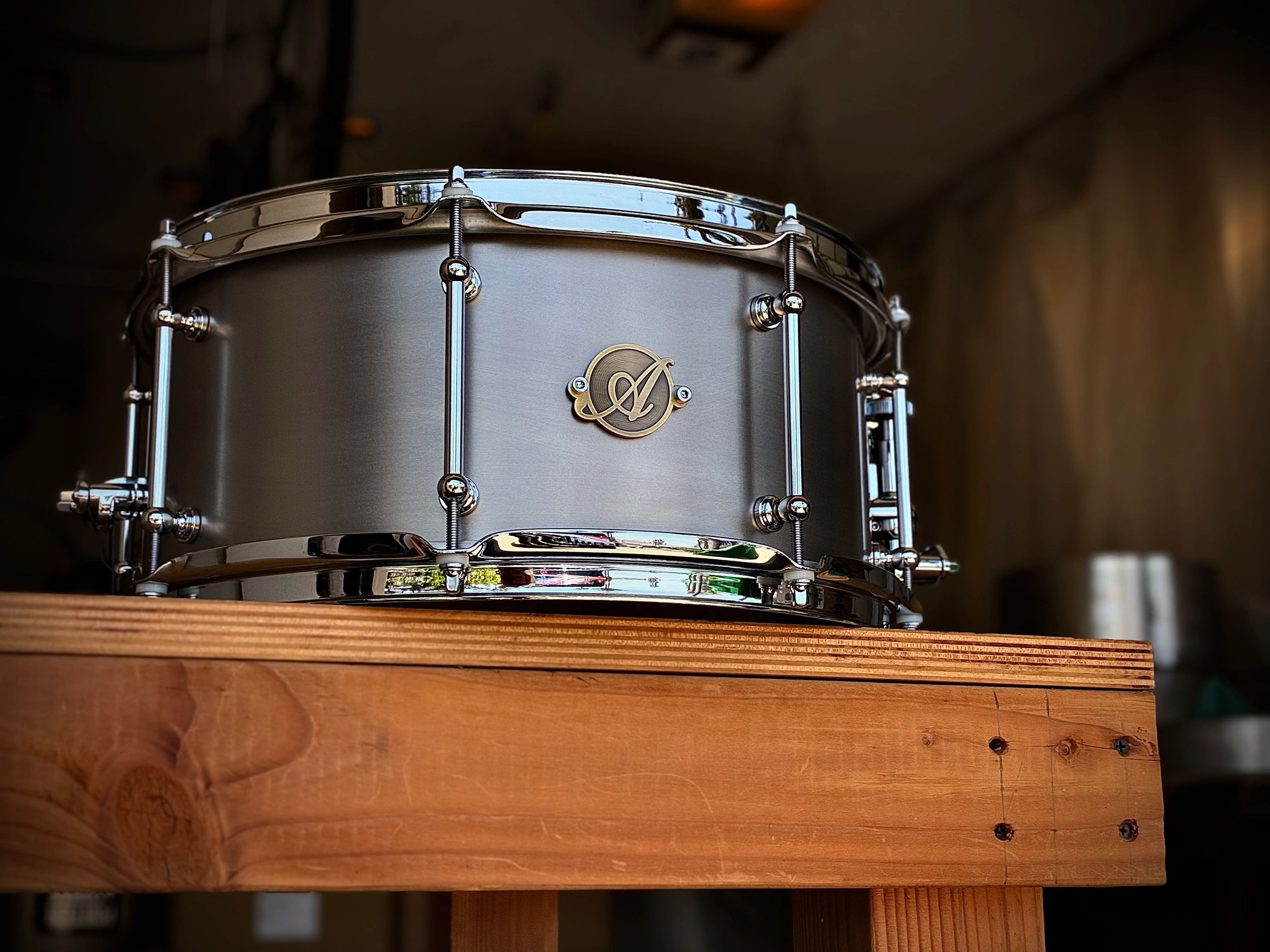 Close-up of a shiny silver snare drum on a wooden surface.