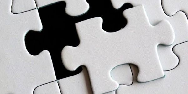 White puzzle piece about to fit into a nearly completed puzzle.