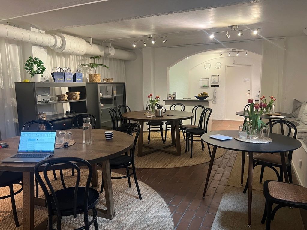 Mötesrum/fikarum med runda bord, svarta stolar och tegelgolv. Tulpaner och laptop på bord. Bra ljus.