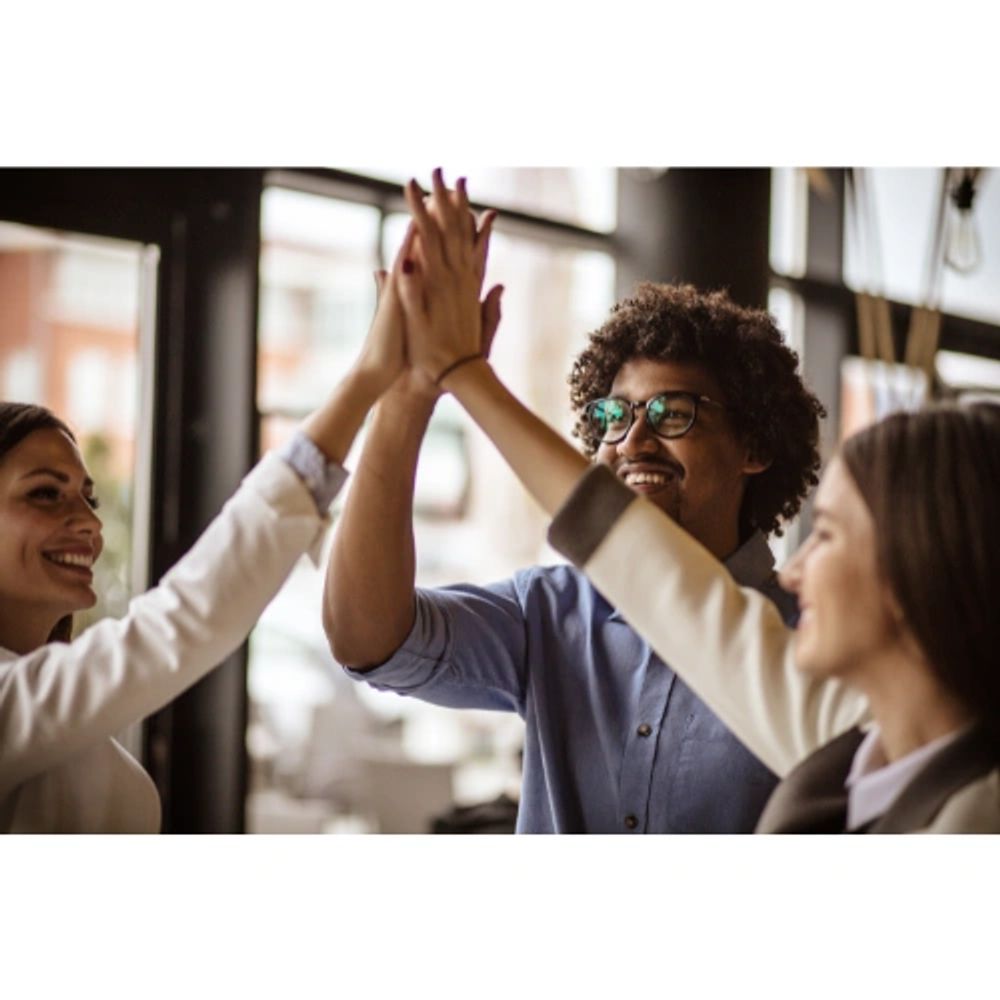 Three colleagues happily giving a group high-five in an office.