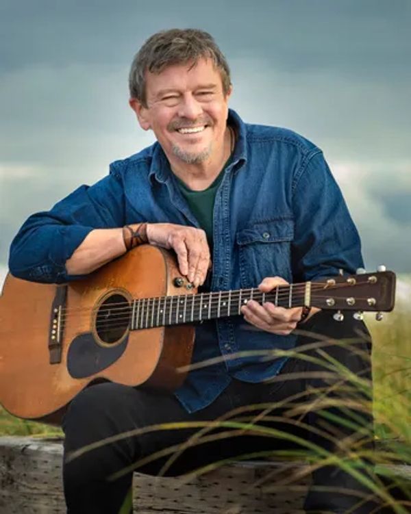 Man smiling while holding an acoustic guitar outdoors.