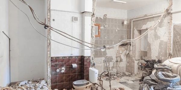 Partially demolished bathroom with exposed wiring and debris.