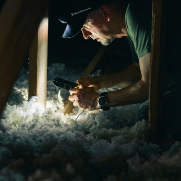 Man inspecting attic insulation with flashlight.