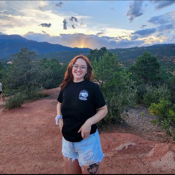 Smiling woman in black shirt and shorts outdoors at sunset.