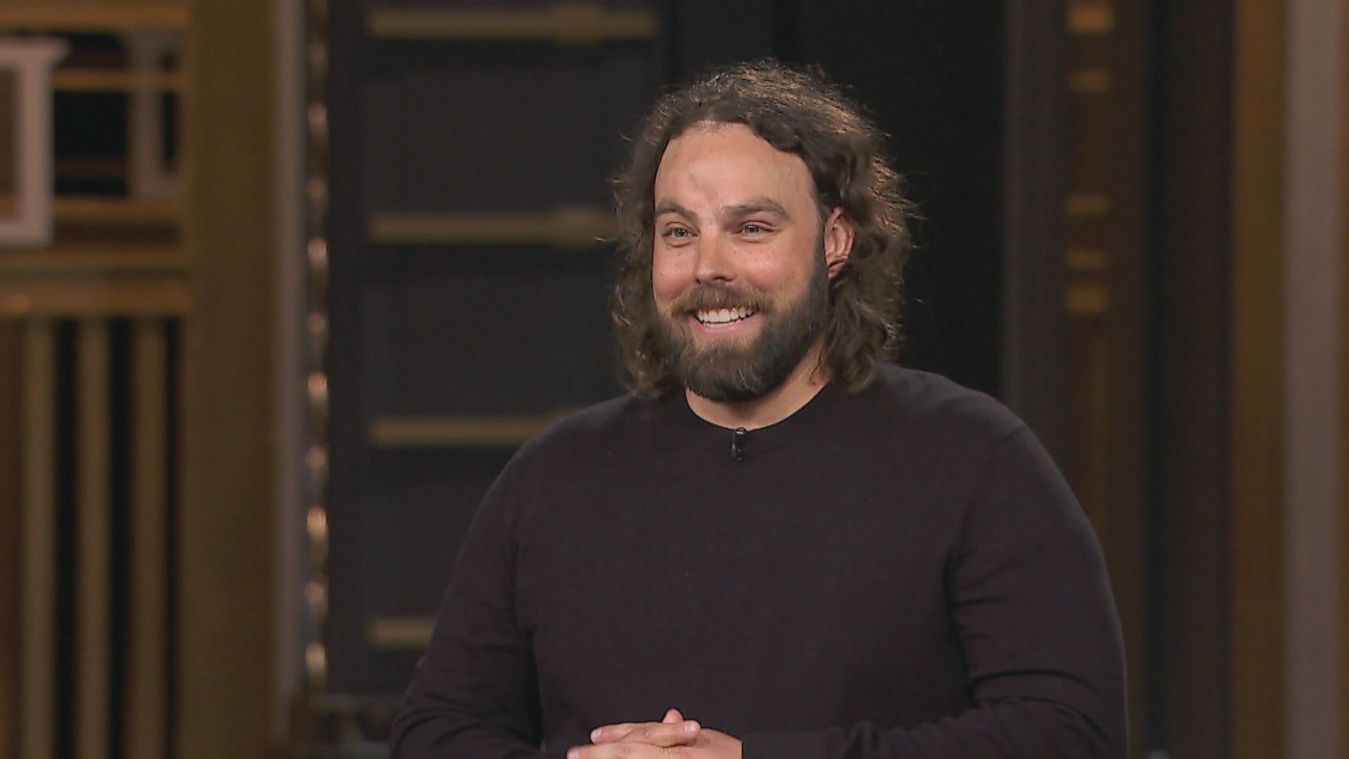 Smiling man with curly hair and beard in black shirt.